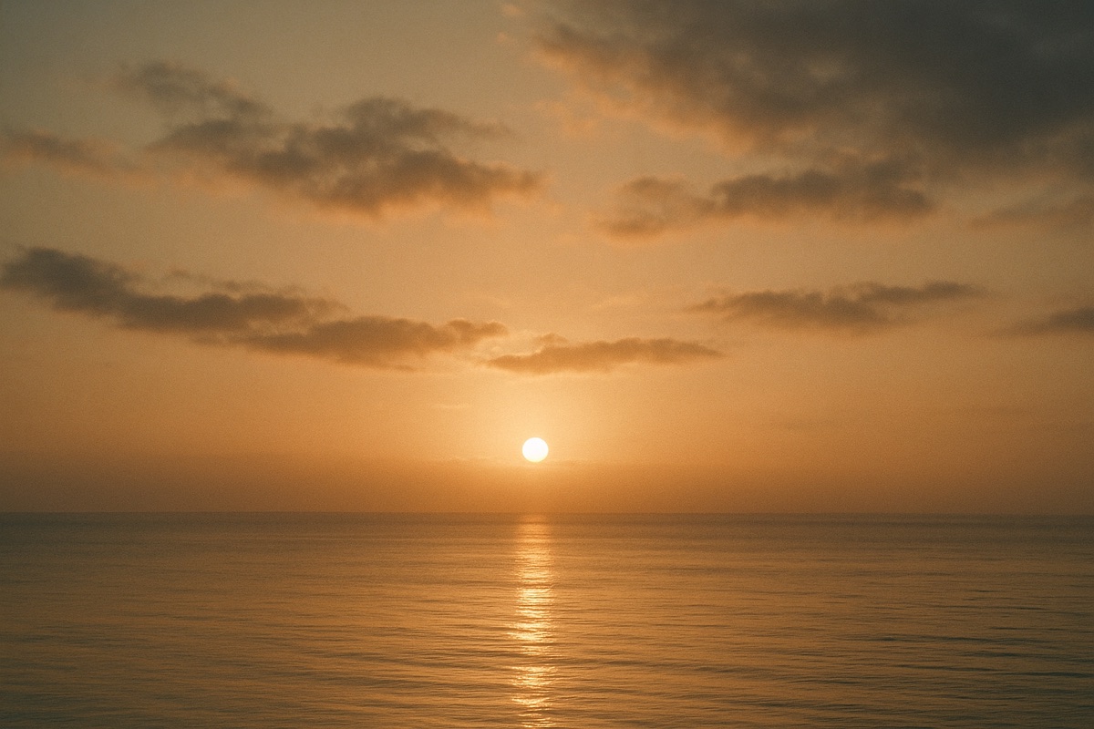A warm sunrise breaking through soft clouds over a calm horizon.